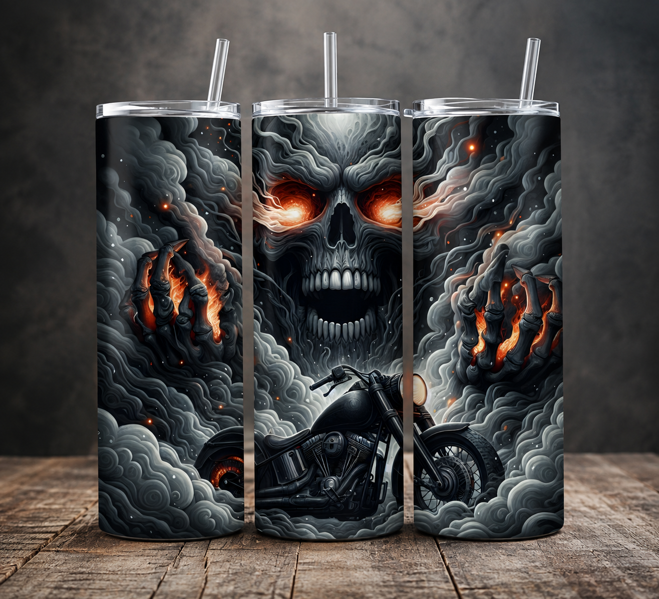 Three tall insulated tumblers with clear straws are shown standing on a wooden surface against a dark gray wall. The tumblers feature a dramatic black, gray, and white smoky graphic with glowing orange-red eyes on a skull, flaming clouds, and a motorcycle illustration.