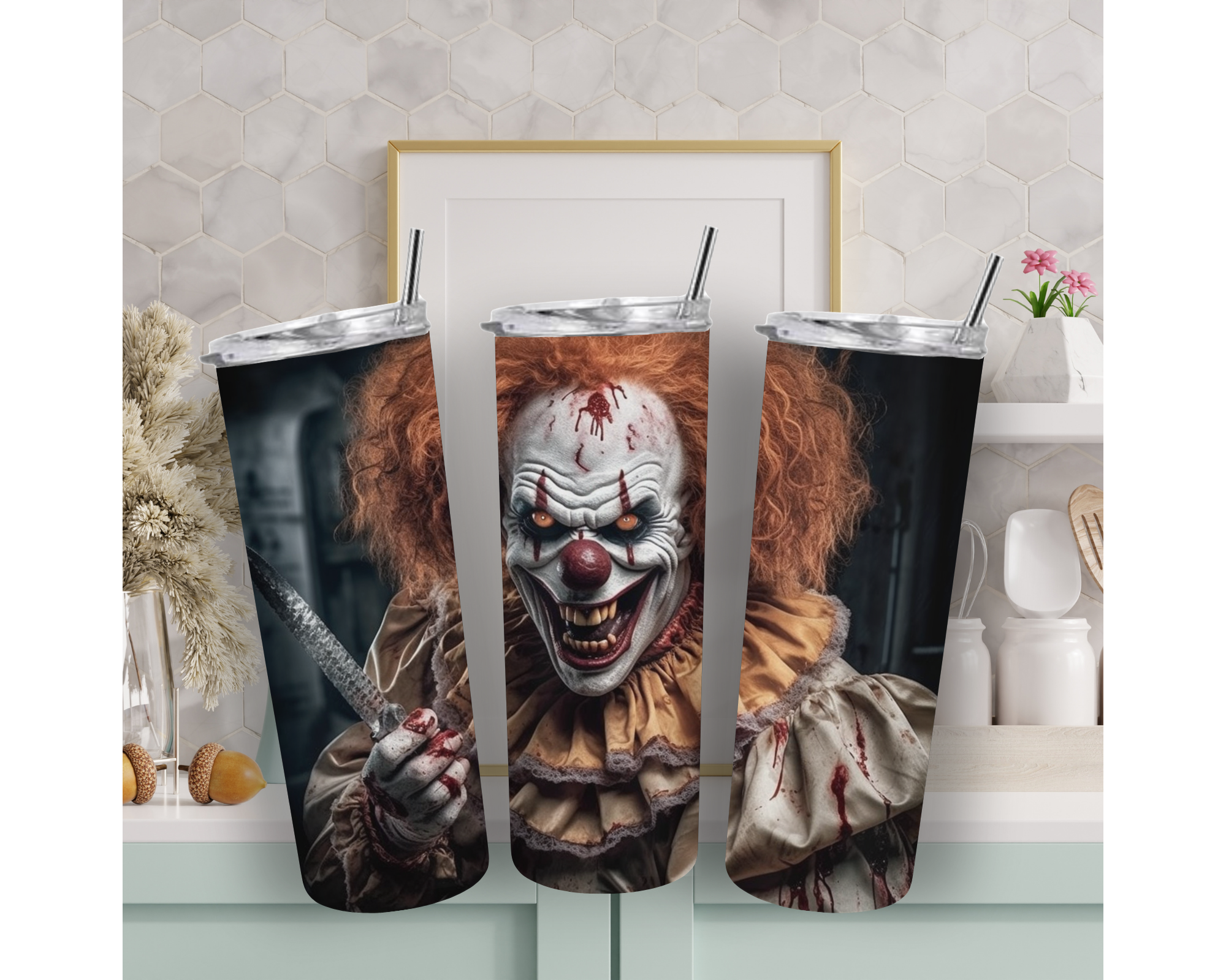 Three tall insulated tumblers with silver lids and black straws, printed with a horror clown design, displayed on a kitchen counter in front of a framed picture.